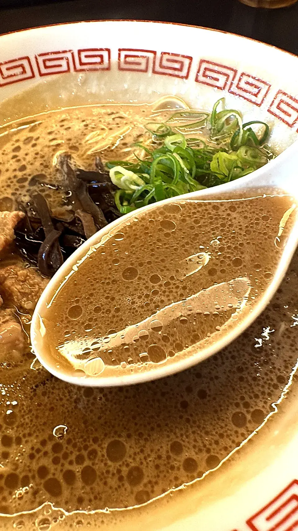 博多とんこつのスープをレンゲですくったところ。泡立つ濃厚な豚骨スープ