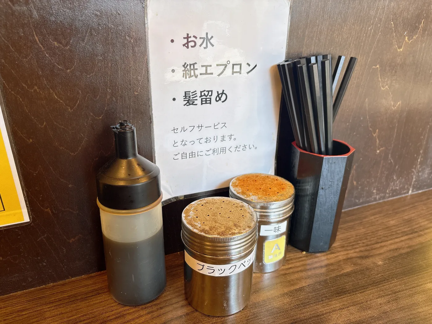 ラーメン つづきの卓上調味料。一味とブラックペッパー、カエシのボトルが並ぶ