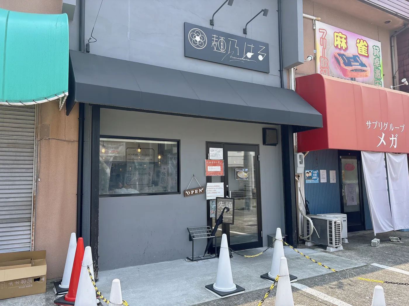 麺乃はるの店構え。グレーの外観に「麺乃はる」の看板、OPENの札と「先頭」の立札