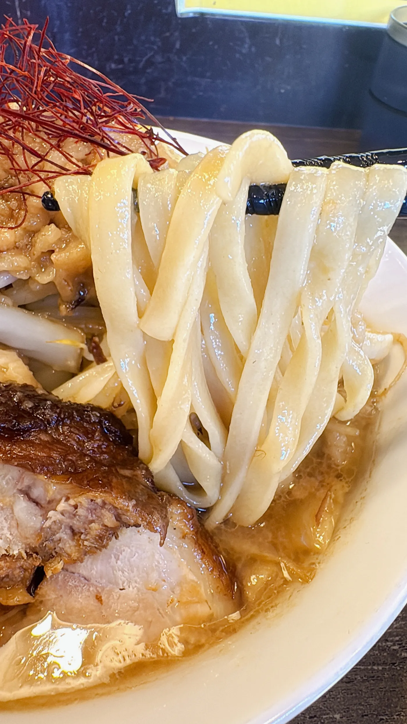 ラーメンつづきの麺を箸でリフトしたところ。平打ち麺