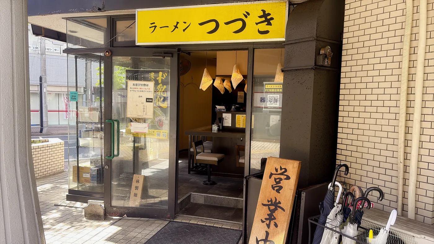 ラーメンつづきの店構え。黄色い看板に「ラーメン つづき」の文字、ドアには「ド乳化」の貼り紙と林製麺のシールが見える