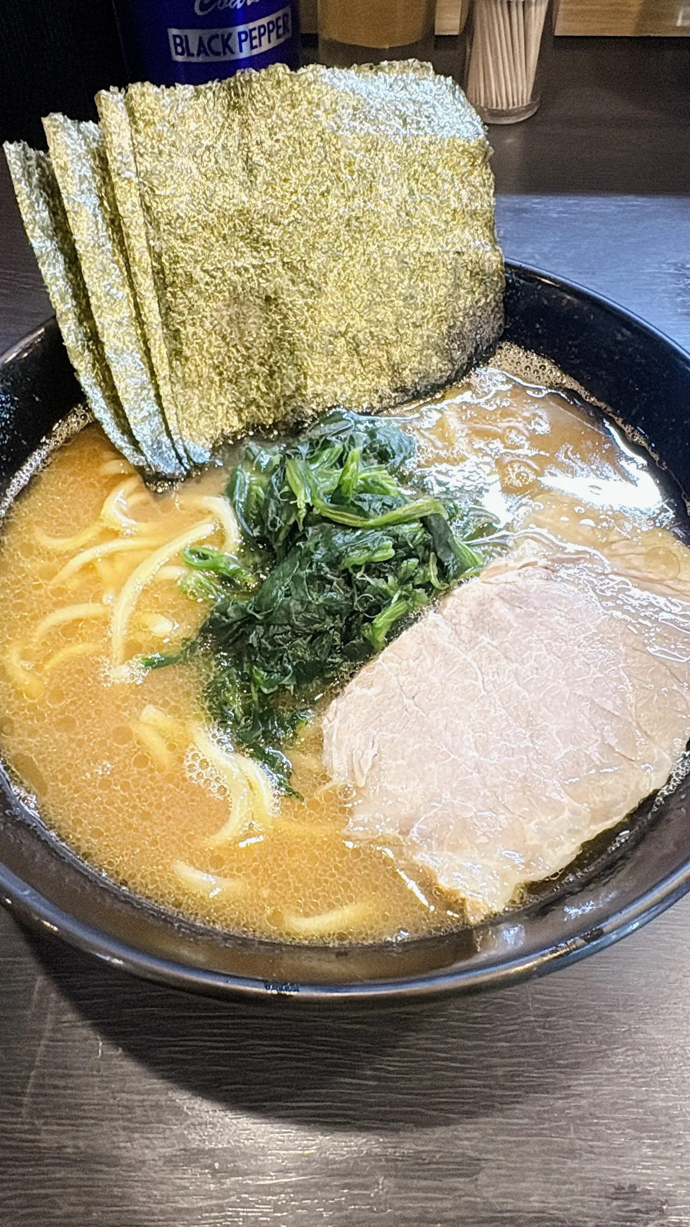 横浜家系ラーメン 侍のラーメンを上から見たところ。黒い器に海苔、ほうれん草、チャーシューがのっている