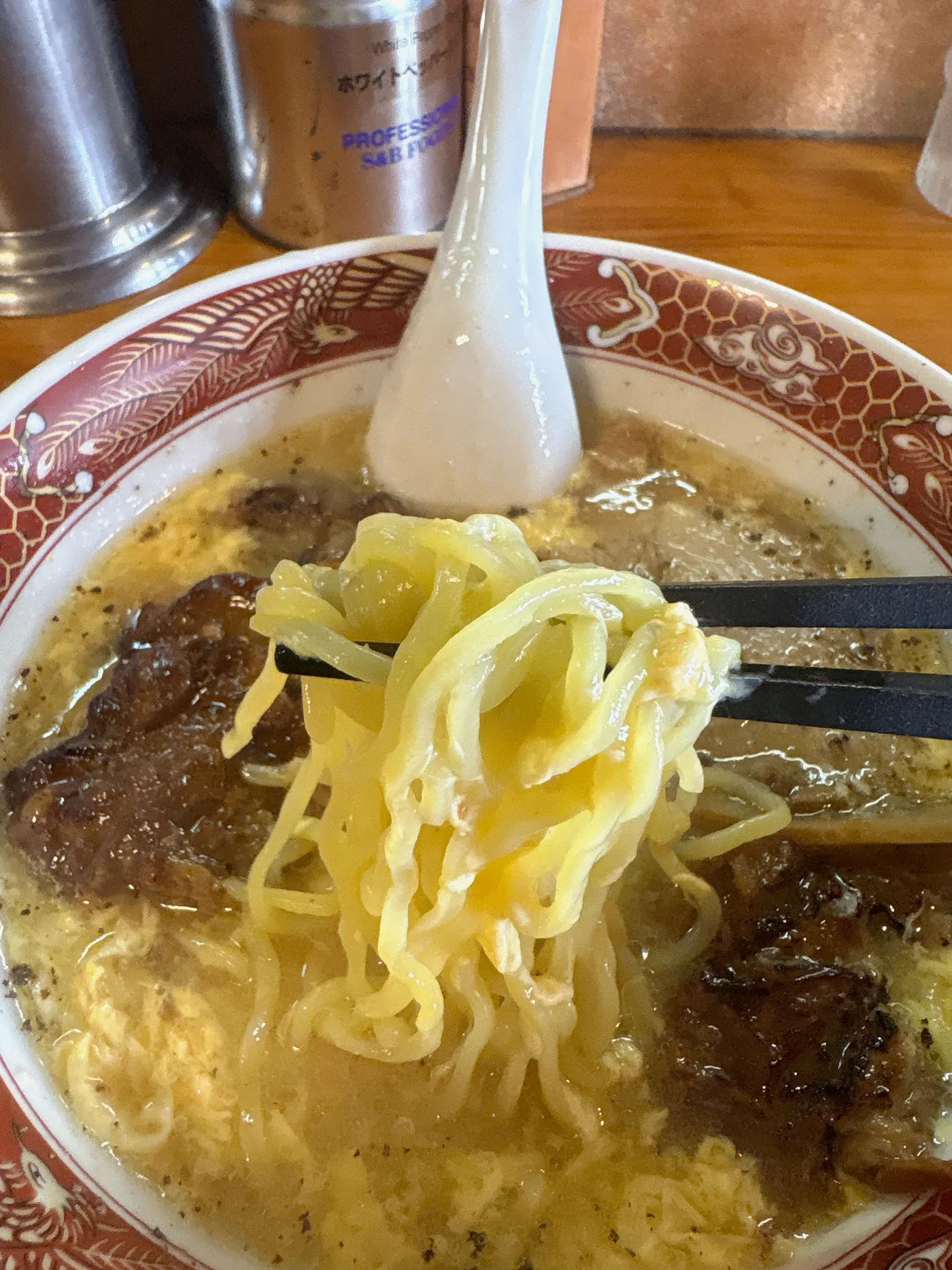 臺大の麺を箸で持ち上げたところ。黄色みのある中太麺に卵とじスープがからむ