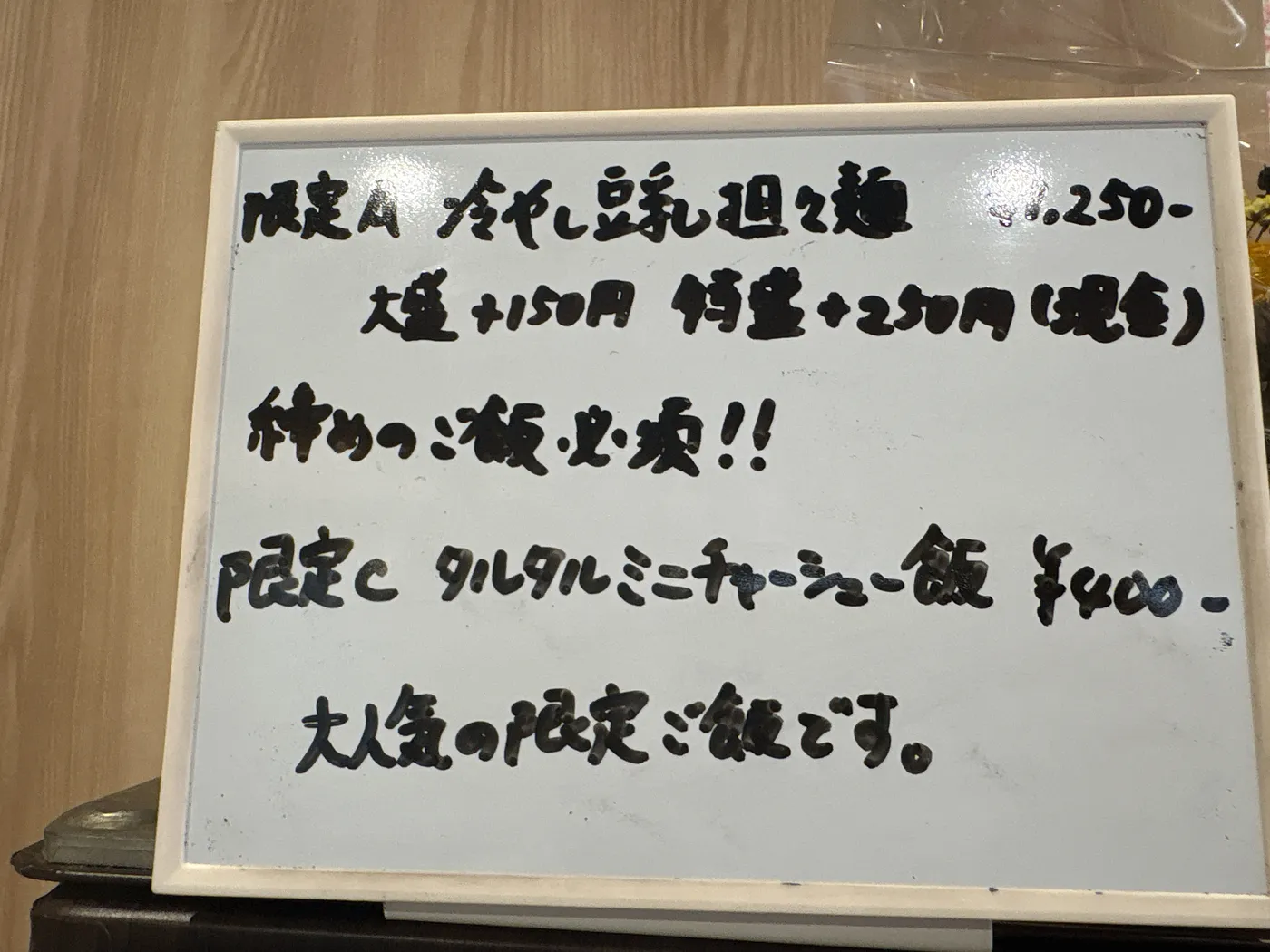 麺屋 伊藤の店内ボード。限定A 冷やし豆乳担々麺1,250円、大盛+150円、特盛+250円、締めのご飯必!!、限定C タルタルミニチャーシュー飯400円と手書きされている