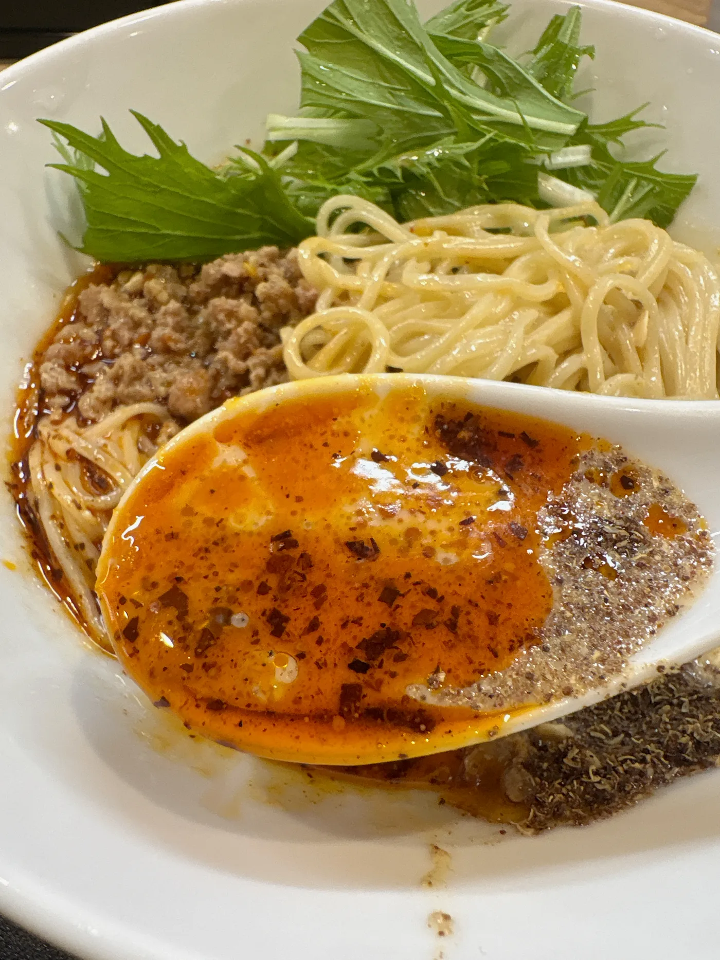 レンゲですくった冷やし豆乳担々麺のスープ。豆乳の白にラー油の赤と唐辛子が混ざり合っている