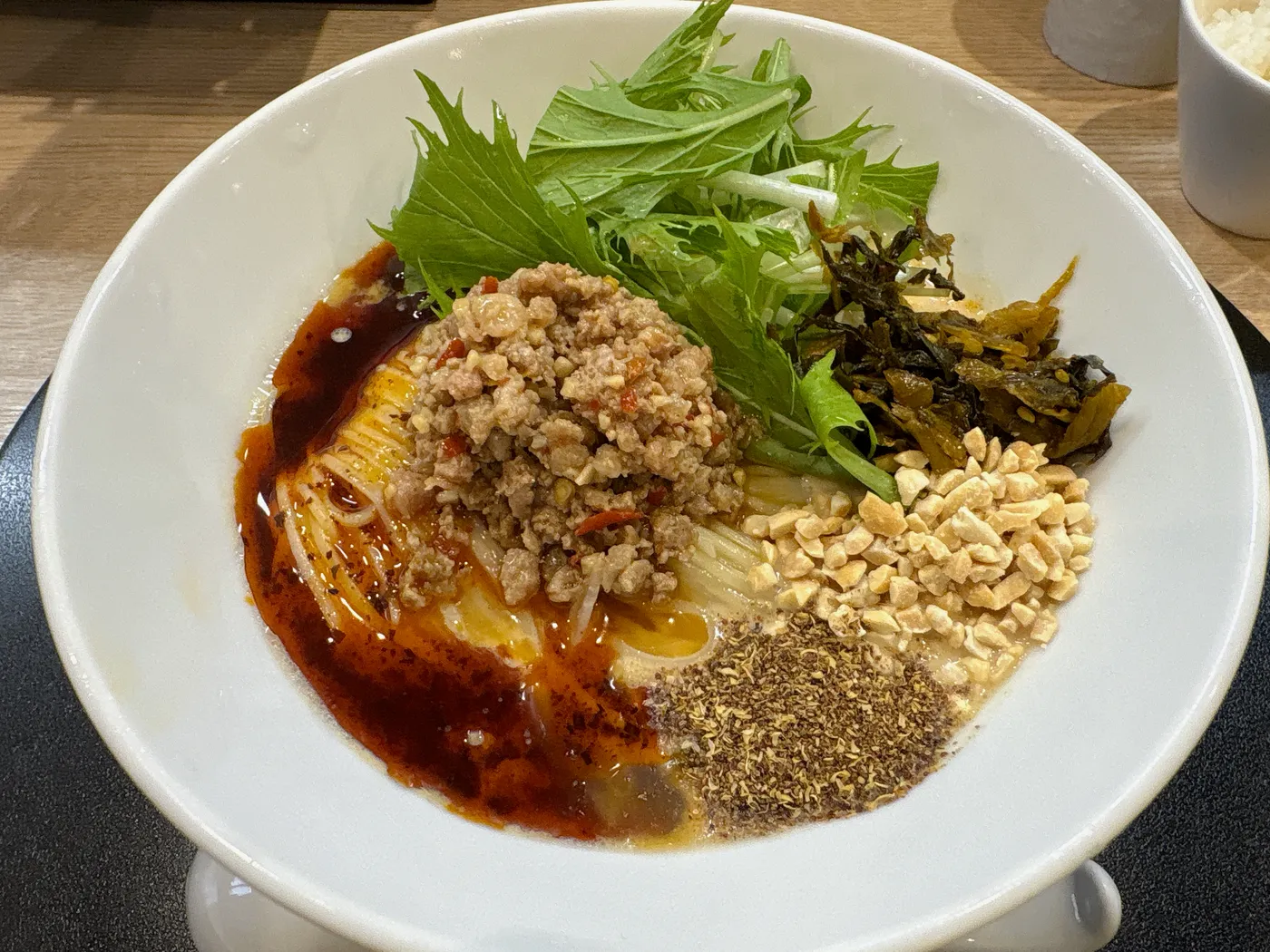 麺屋 伊藤の限定・冷やし豆乳担々麺。白い豆乳スープの上に赤いラー油が流れ、ミンチ、ナッツ、山椒、水菜がのる
