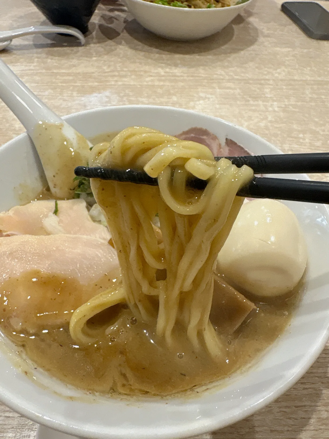 麺屋 伊藤の特製鶏白湯醤油ラーメンの麺を箸で持ち上げたところ。中太のストレート麺に濃厚なスープが絡む